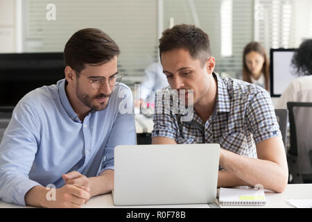 Focused serious male coworkers talking working together on compu Stock Photo