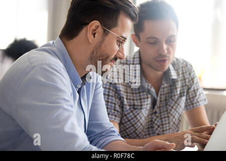 Focused male colleagues work together using laptop discussing on Stock Photo