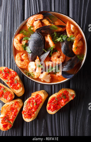 Bouillabaisse soup with seafood and fish close-up in a bowl served with toasts on the table. Vertical top view from above Stock Photo