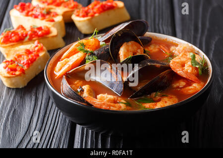 Traditional recipe for French bouillabaisse soup with seafood and fish close-up in a bowl served with toasts on the table. horizontal Stock Photo