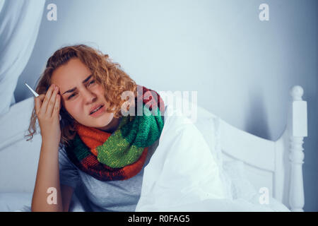 Sick blonde girl is scarf touches her head. In bed Stock Photo