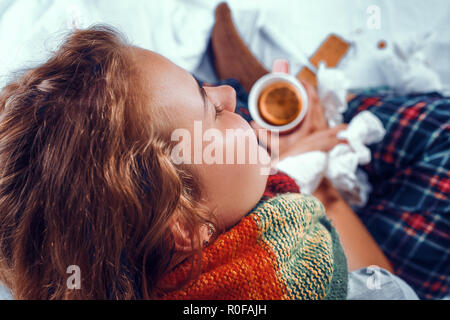 View from above on sick woman in bed holding a cup of tea with orange in it Stock Photo