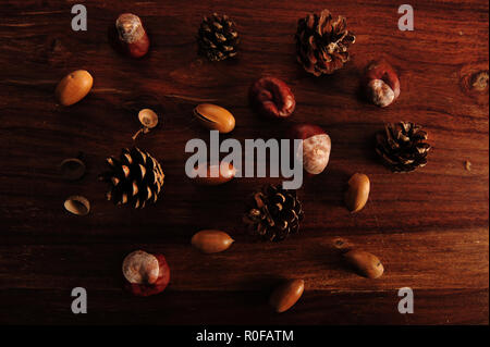 Chestnuts, acorns and pine cones spread out on dark brown wooden table surface. Horiontal photo. Stock Photo