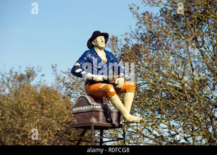 Model of poorly-dressed man sitting on trunk, with pistol in his hand, as 'Point of Sale' display outside closed shop, Hayling Island England Stock Photo
