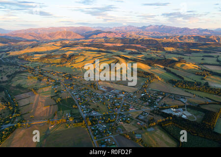 The view from above in a hot air balloon of a town, surrounding hills, mountains, and the farm fields below in the early morning light