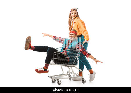 cheerful hipster girl carrying shopping trolley with happy boyfriend with wide arms isolated on white Stock Photo