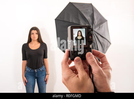 Attractive woman posing for her passport photo in a photographic studio with the photographers hands in the foreground holding the camera with viewfin Stock Photo