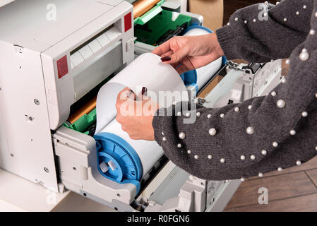 Woman adjusting a roll of new photo paper on a photographic printer in a printing house or studio in a close up view of her hands Stock Photo