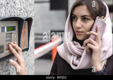 brunette woman calls into the intercom on the street, autumn day in warm clothes Stock Photo