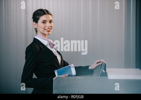 young female worker smiling at camera while working at check-in desk in airport Stock Photo
