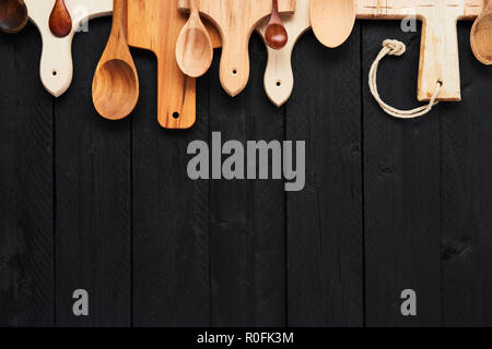 Top view of assorted wooden spoons and chopping boards on black wooden table with copy space. Food background concept. Stock Photo