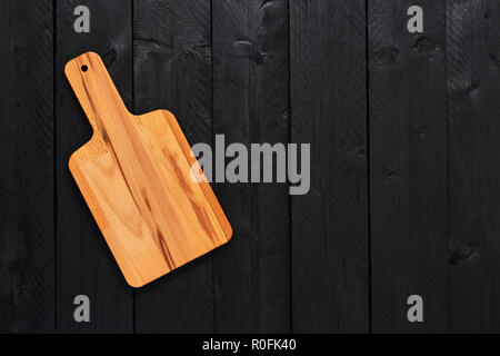 Top view of small solid beech wood chopping board on black wooden table with copy space. Stock Photo