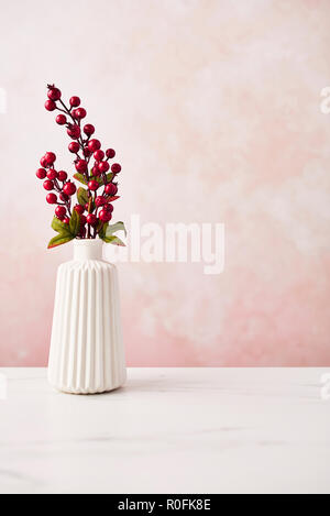 Artificial interior decoration. Twig with berries in the vase on white marble table over pink wall background. Copy space. Stock Photo