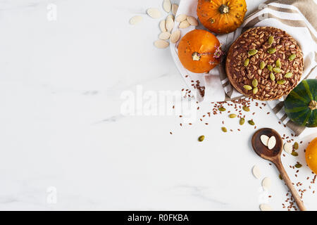 Top view of autumn whole wheat bread on white marble table with pumpkins, seeds, flax and wooden spoon on white marble table. Copy space. Stock Photo