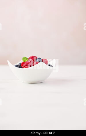 Fresh blueberries and raspberries with mint leaf in white bowl on white marble table over rose background with copy space. Stock Photo