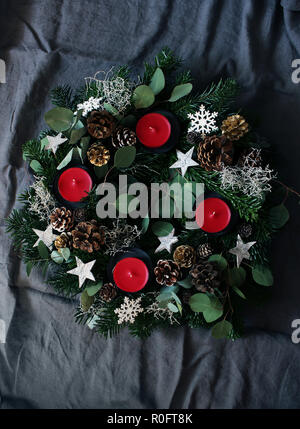 Christmas composition of advent wreath on dark grey table linen background. Made of evergreen fir tree branches, eucalyptus leaves, snowflakes, golden and natural pine cones. Flat lay, top view. Stock Photo