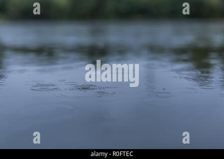 Calm rain drops on the surface of water in a puddle with graduated shade of black shadow and reflection of blue sky Stock Photo
