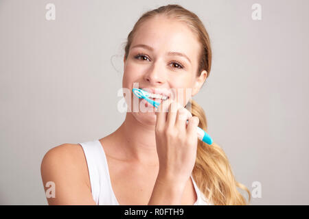 Portrait of young woman brushing her teeth while standing at isolated background. Stock Photo