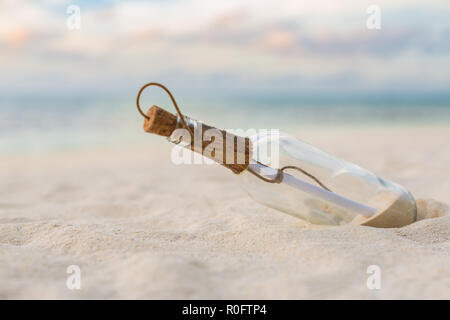 Message in the bottle washed ashore against the sun setting down. Tropical beach design background Stock Photo