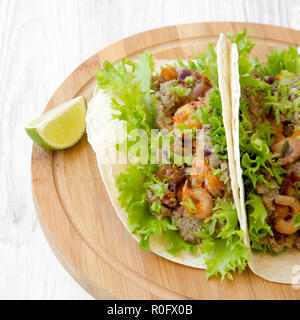 Shrimp tacos on round bamboo board on white wooden background, side view. Mexican food. Closeup. Stock Photo