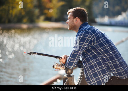 young fisherman with rod and sunglasses fishing in lake Stock Photo