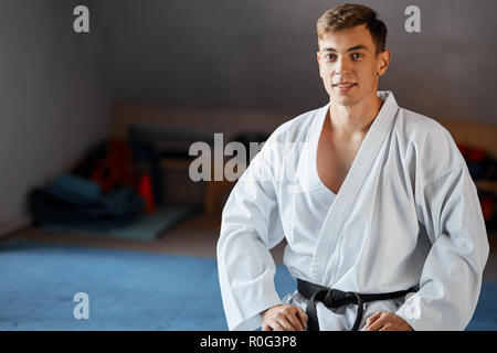 Karate man in kimono sits on knees on floor in martial arts gym Stock Photo