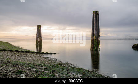 Large supports from long gone structures sit in a pacific northwest bay. Long exposure smooths the water and sky to a misty bliss Stock Photo