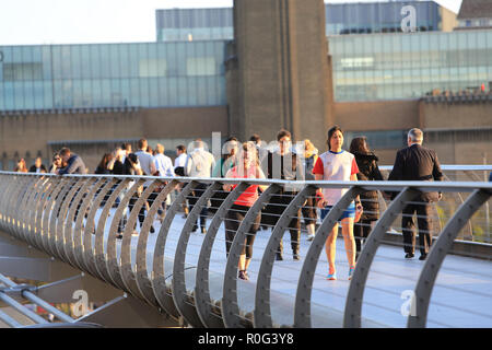 People crossing the Millennium Bridge on a bright spring day in the late afternoon, in central London, UK
