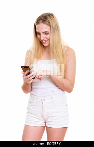 Studio shot of young happy teenage girl smiling while using mobi Stock Photo