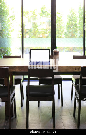 Laptop blank screen of white color placed on a table in a restaurant and have coffee cup places nearby for design in your work. Stock Photo