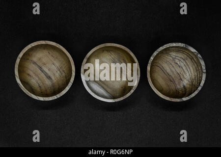 Three brown bowls made from palm tree wood placed in line on black background Stock Photo