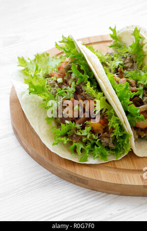 Shrimp tacos on round bamboo board on white wooden background, side view. Mexican cuisine. Stock Photo