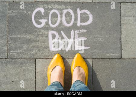 Female feet with text goodbye written on asphalt. Stock Photo