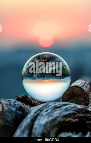 Scenic autumn sunset in Caucasus mountains viewed through glass ball lying on wood pile. Vertical scenery with blurred background Stock Photo