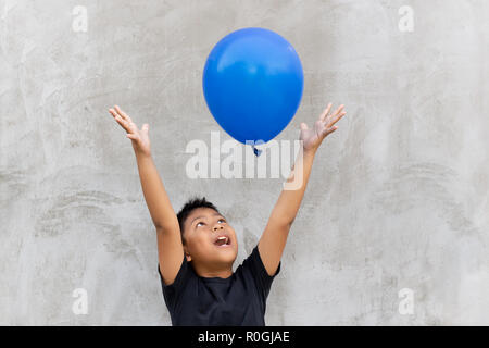 Asian boy play catches balloon on grey background. Stock Photo