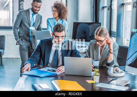 multicultural businesspeople looking at laptops in office Stock Photo