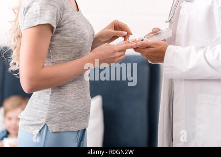 cropped shot of pediatrician giving pills to mother for ill kid lying in bed blurred on background Stock Photo