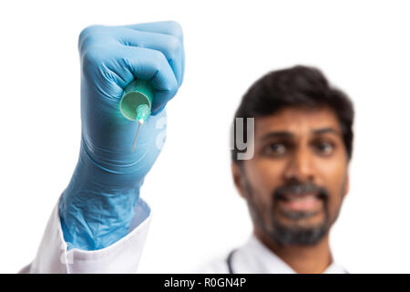 Indian male doctor or medic vaccinating with focused expression wearing latex gloves close-up isolated on white background Stock Photo