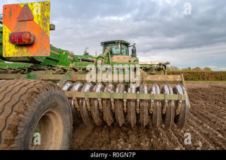 Close up of a plough behind a large tractor getting a farm field ready for new crops Stock Photo