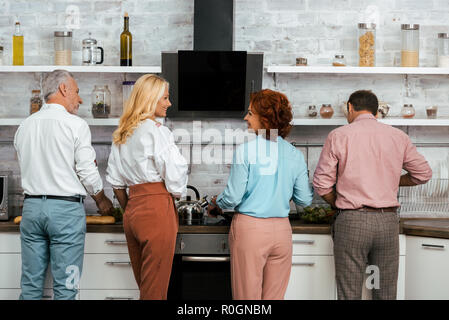 back view of mature friends talking and cooking together in kitchen Stock Photo