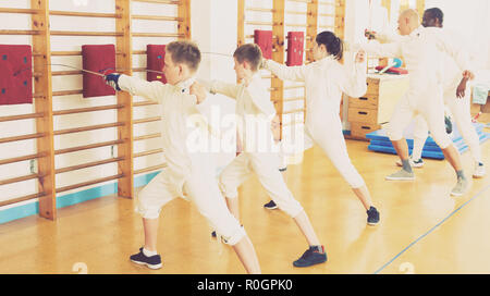 Kids with adults practicing effective techniques of fencing in gym Stock Photo