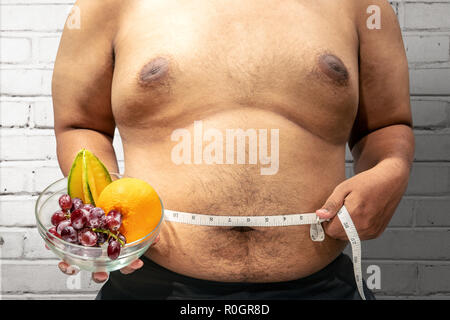 Fat man diet with fruit using measuring tape to measuring his stomach at home. Fat man diet Stock Photo