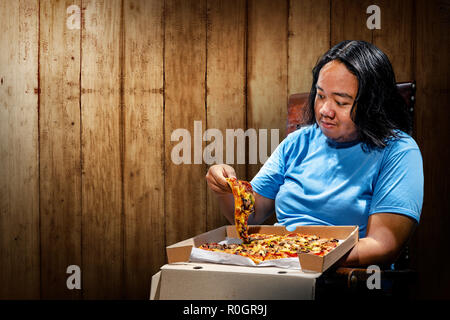 Young asian fat man eating slice of pizza on chair. Fat man diet concept Stock Photo