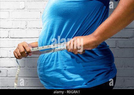 Fat man using measuring tape to measuring his belly at home. Fat man diet concept Stock Photo