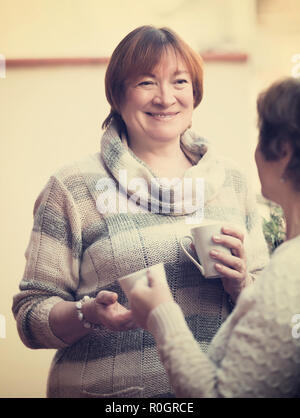 Senior women in pullovers having cup of tea on terrace Stock Photo