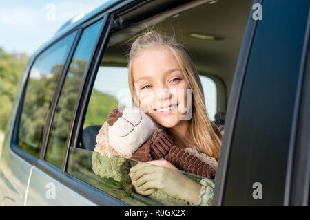 close-up portrait of smiling little child riding car on nature with teddy bear Stock Photo