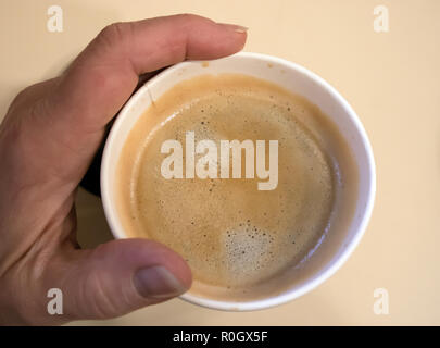 Closeup top view of one-off cup of appetizing morning coffee with foam in senior hand Stock Photo