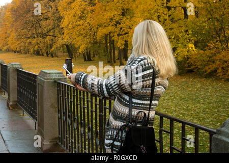 Long haired young blonde woman making selfie against romantic yellowed trees Stock Photo