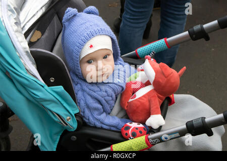 Cute serious baby sitting in stroller dressed in knitted azure costume with red toy in hands Stock Photo