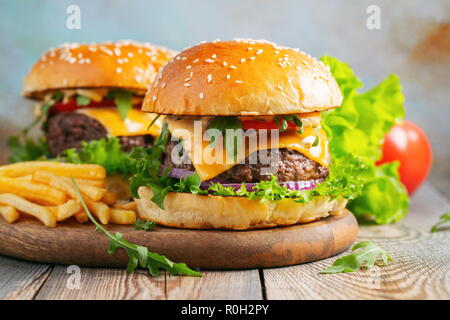 Two fresh homemade burgers with fried potatoes on a wooden table. Stock Photo